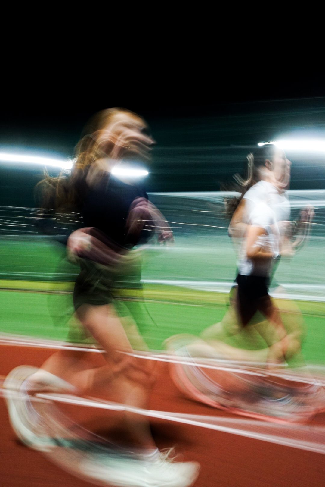 Blurred motion shot of runners racing on a red track at night under stadium lights.