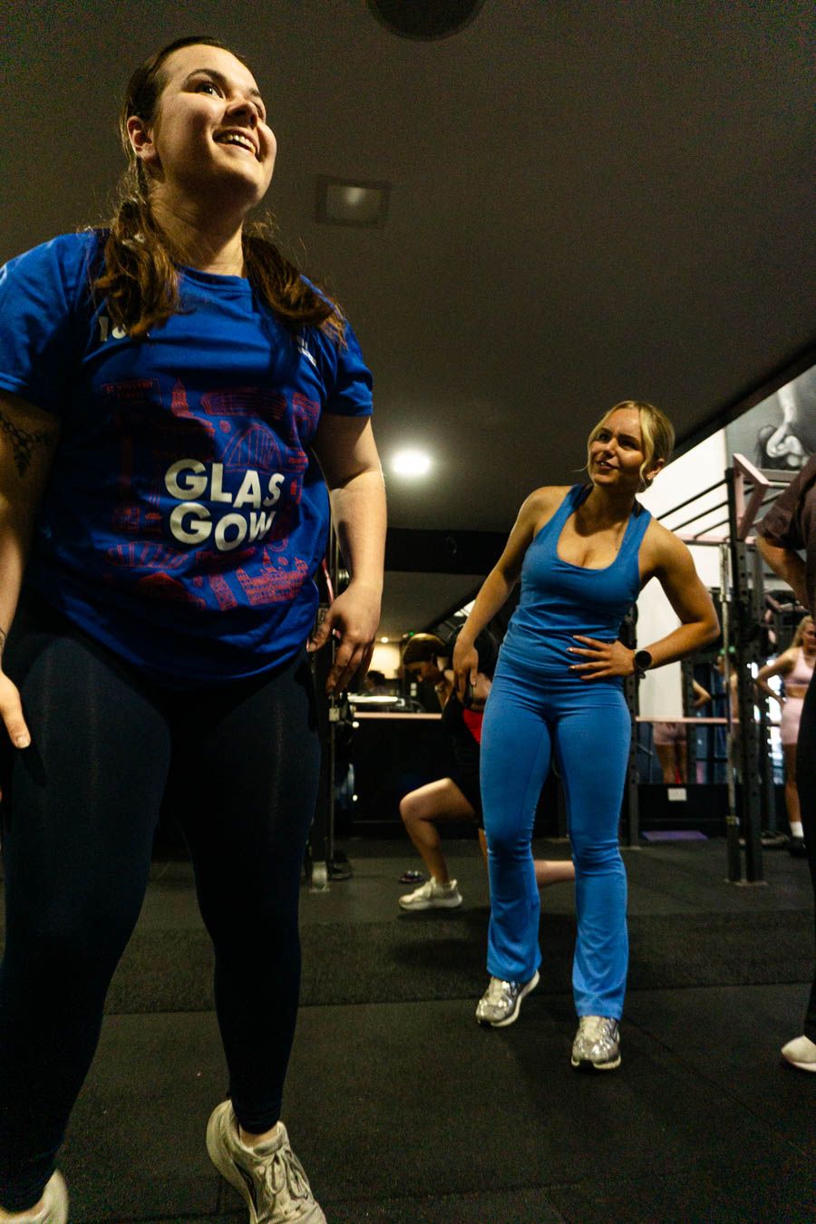 Two women laughing during a fun group fitness workout in a gym.