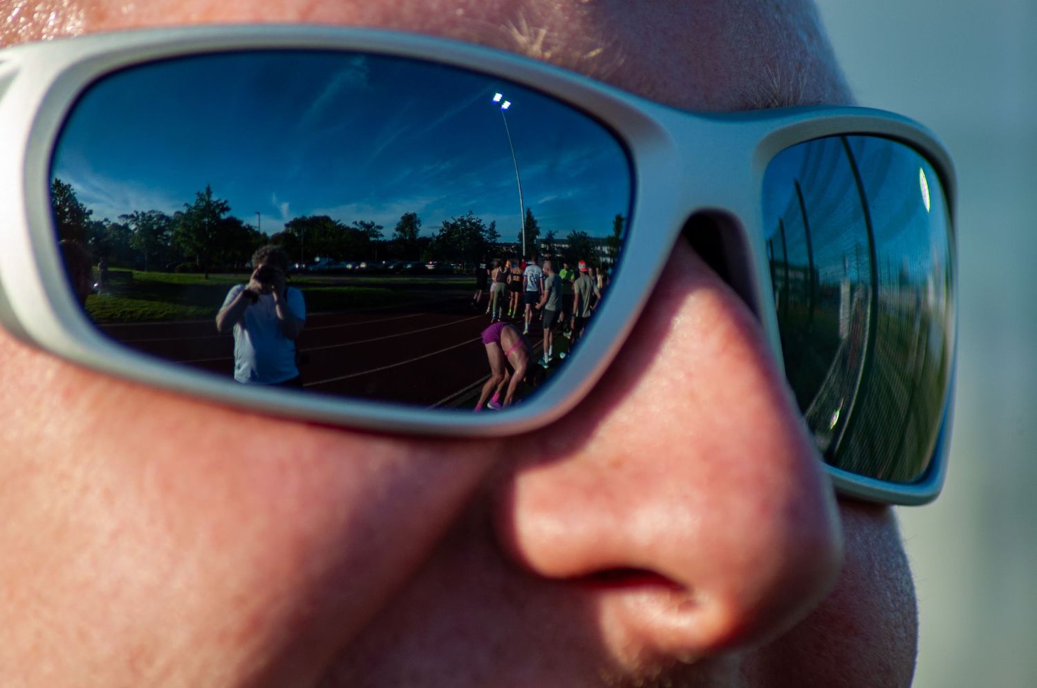 Reflection of athletes at a running track event visible in white sports sunglasses closeup.