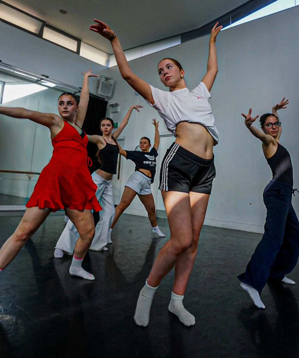 Group of contemporary dance students rehearse energetic routine in mirrored studio wearing casual attire.