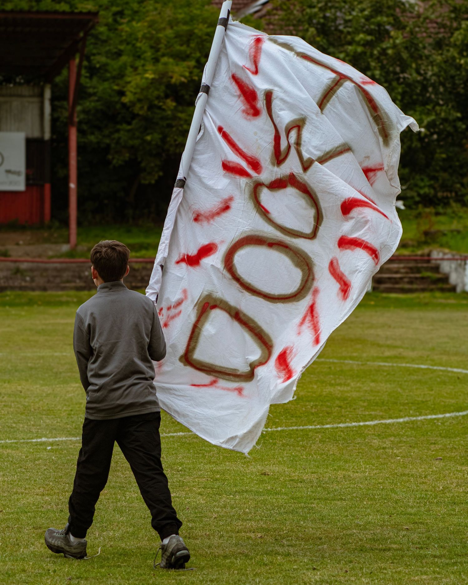 A young boy waves a large handmade white flag with red lettering on a football pitch.