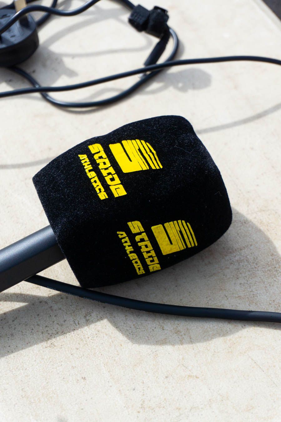 Black microphone with yellow STRIDE Athletics branding logo resting on a light surface.