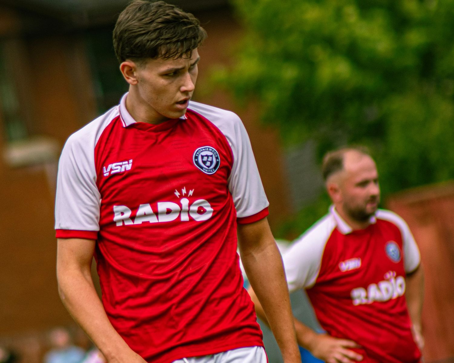 Two soccer players in red and white VSN Radio jerseys during an outdoor match on a green field.