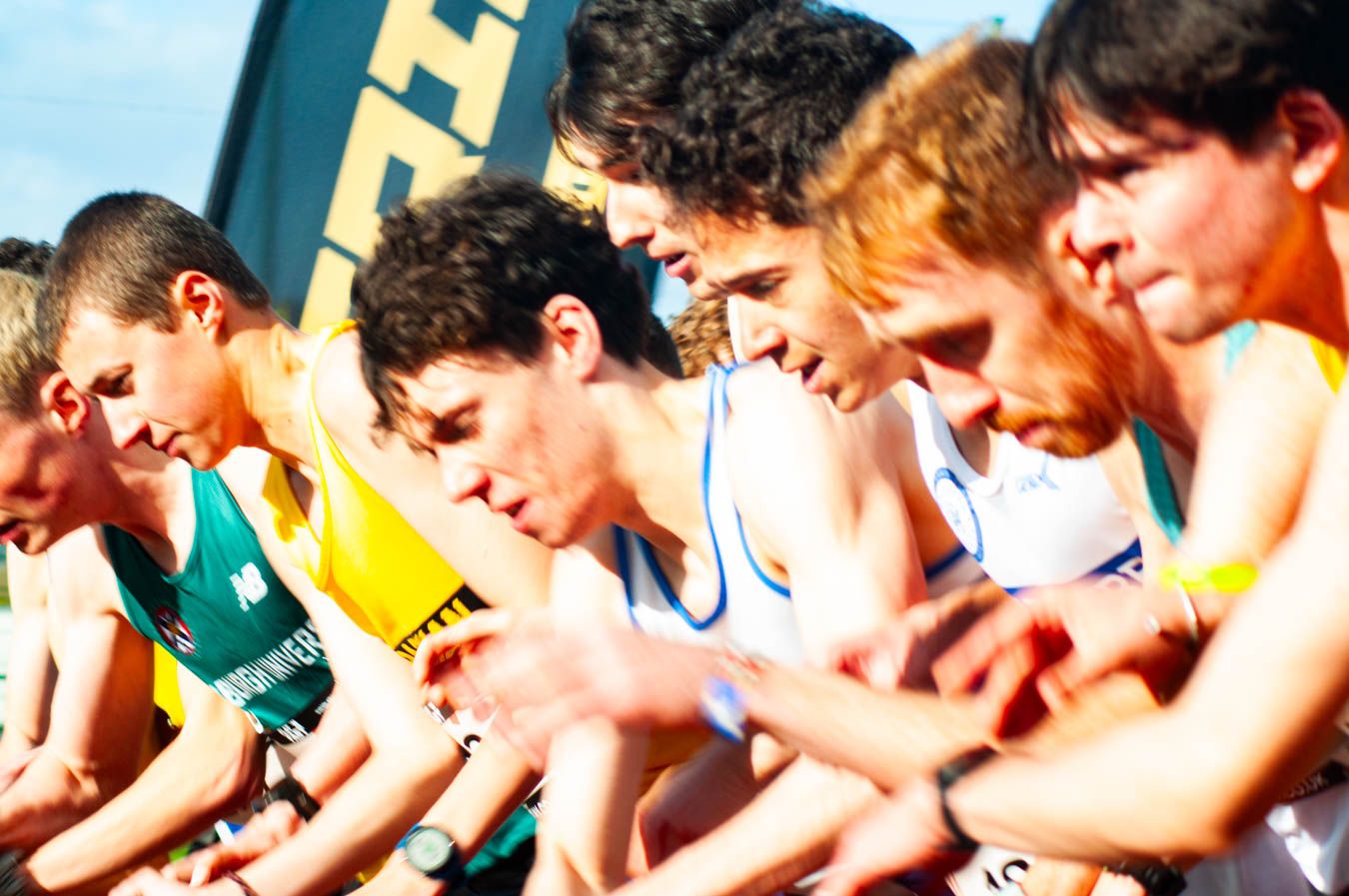Male runners crouched at starting line of competitive outdoor athletics race.