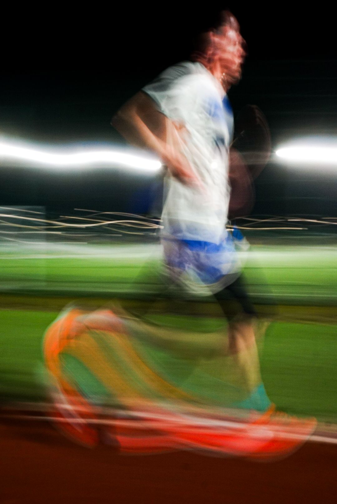 Motion blur action shot of a male runner in blue shorts racing on a track at night.