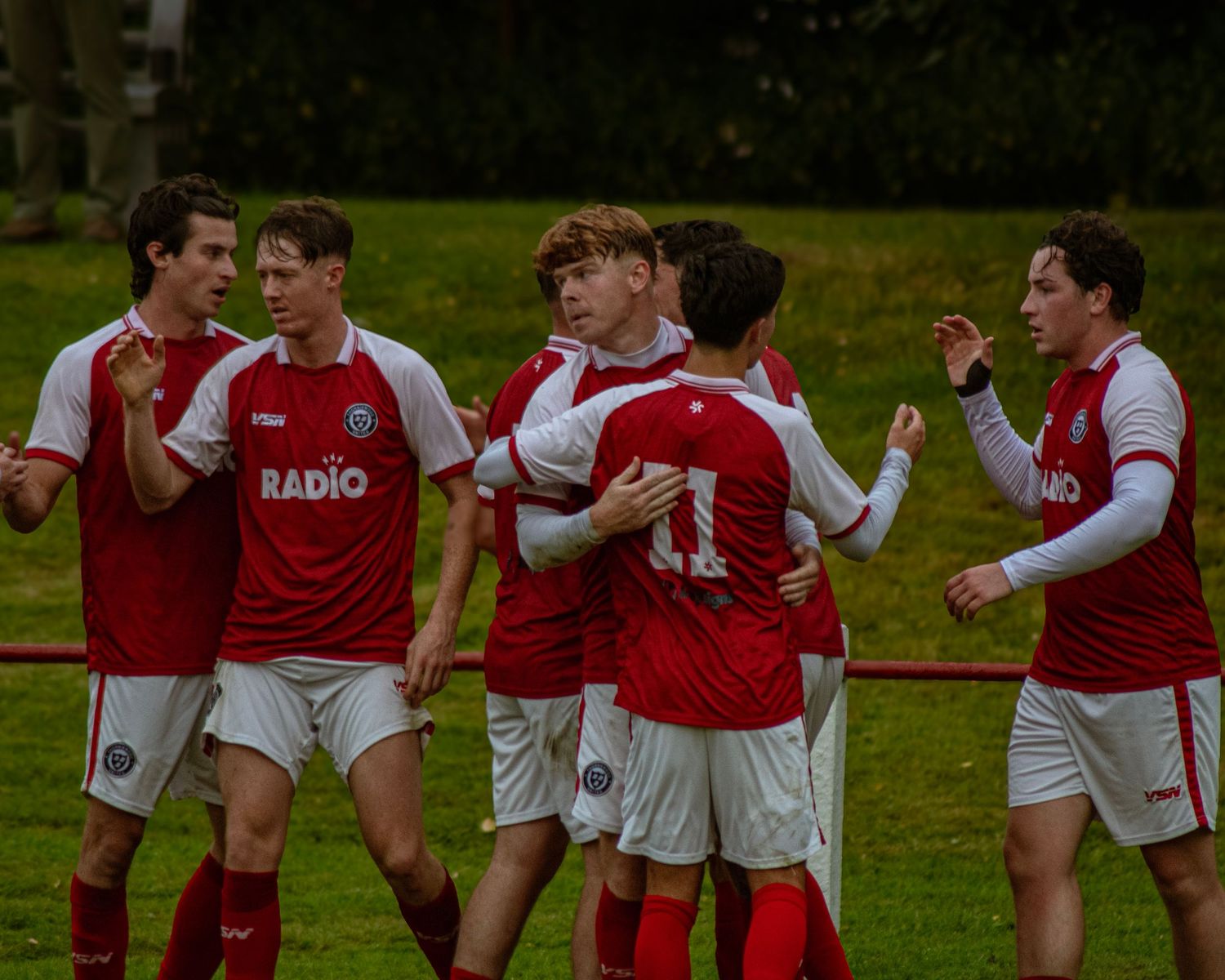 Youth soccer team in red and white jerseys celebrate together on a green field during a match.