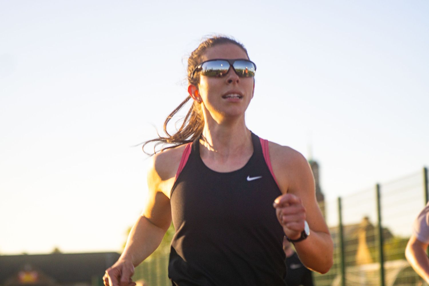 Female runner in Nike tank top and sport sunglasses training outdoors in golden hour light.