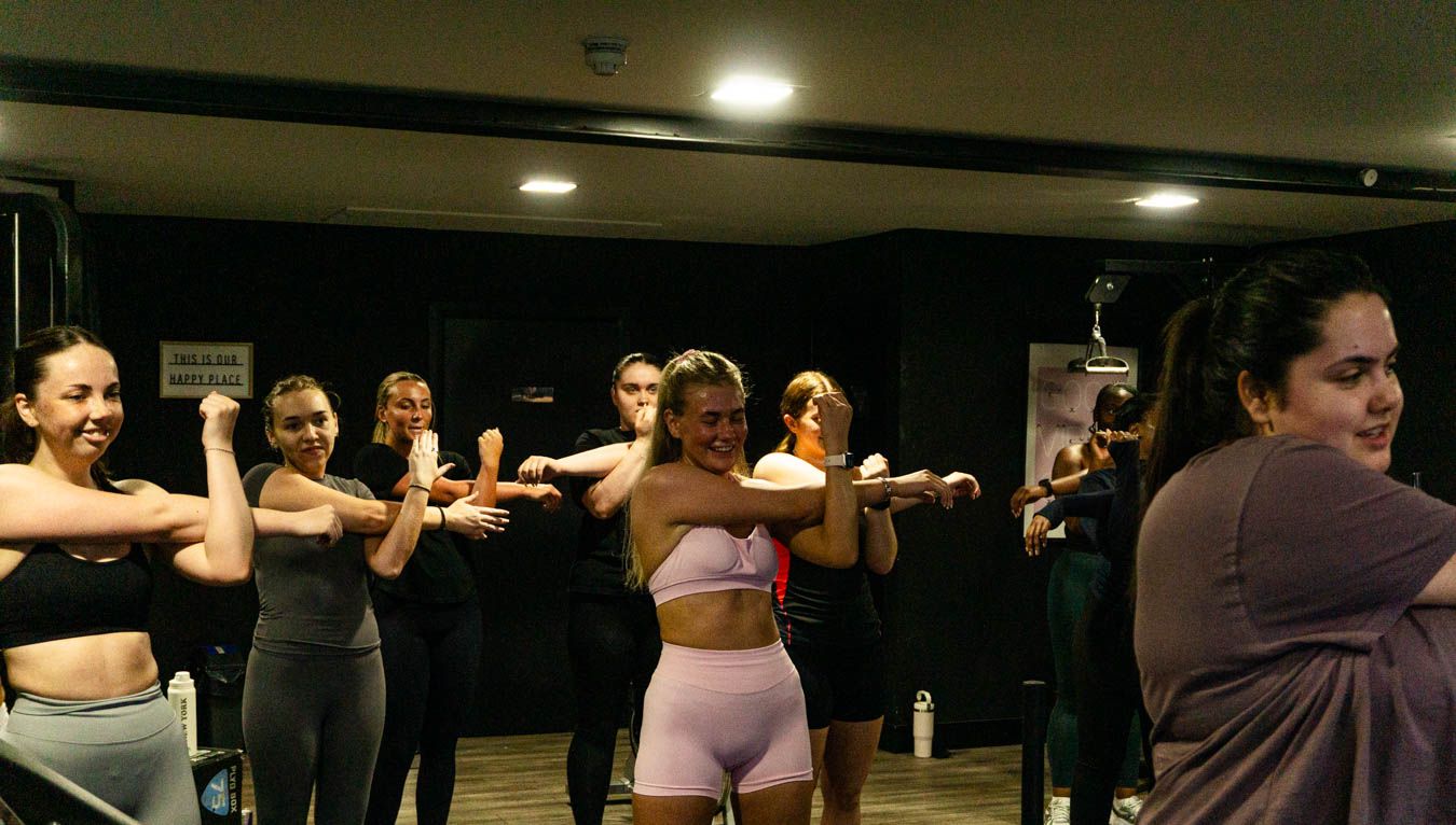Group of smiling women stretching arms forward in a fitness dance class.