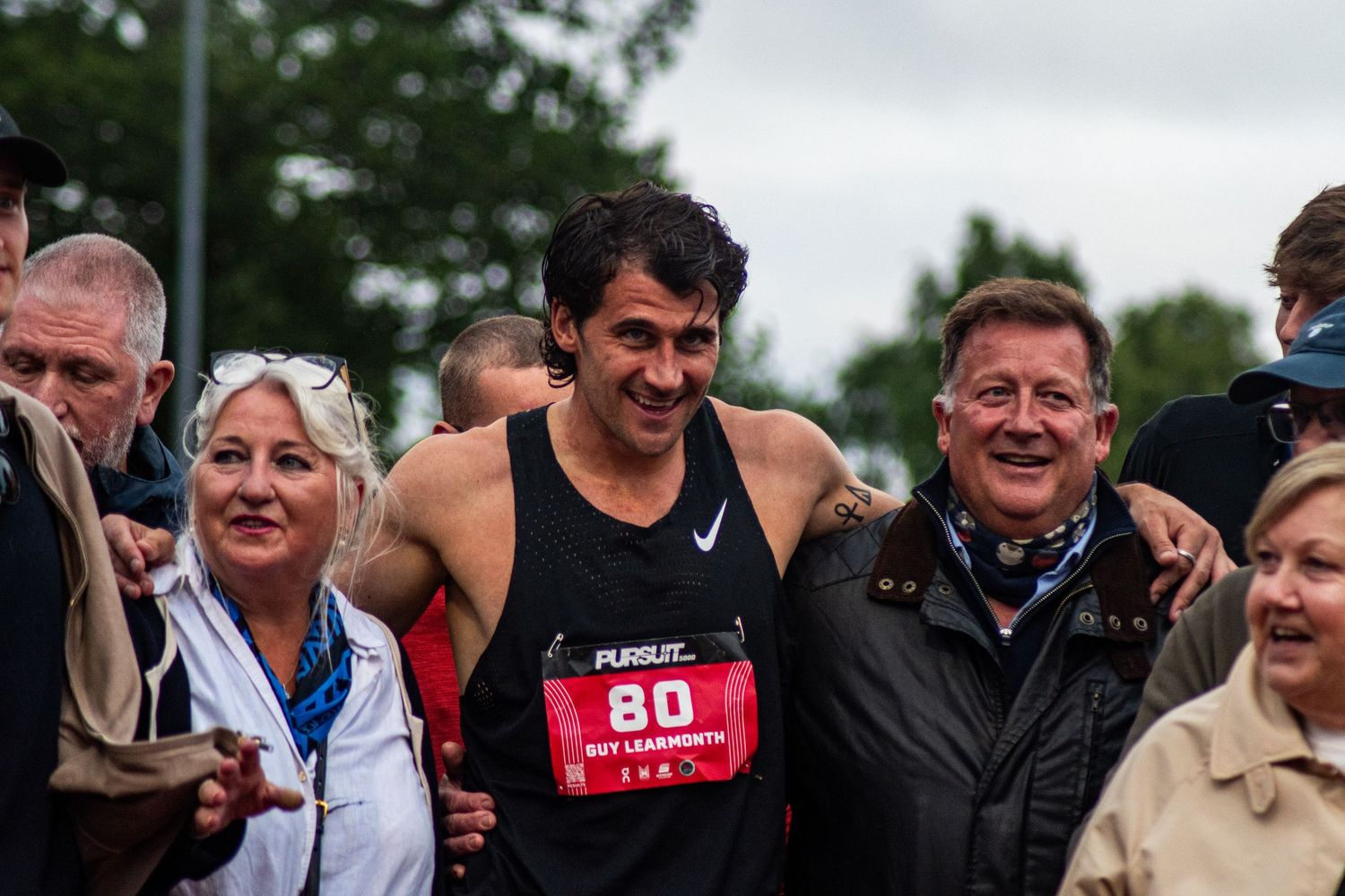 Smiling male runner wearing bib number 80 celebrates with crowd after completing a road race event.