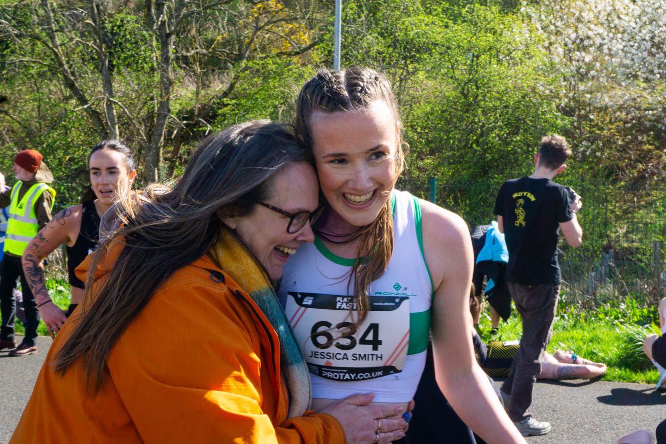 Two women embrace and smile after completing a road race, one wearing bib number 634.