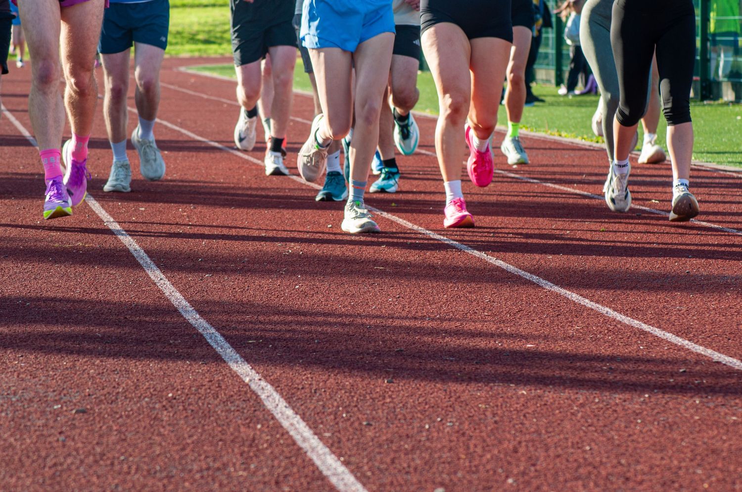 Group of runners racing on a red athletics track wearing colorful shoes.