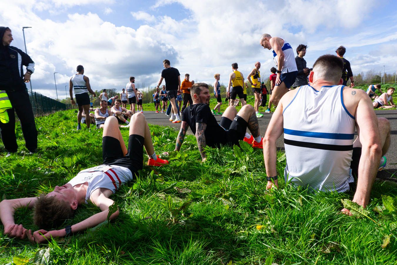 Exhausted runners rest on grass beside a road after completing a tough athletics race event.