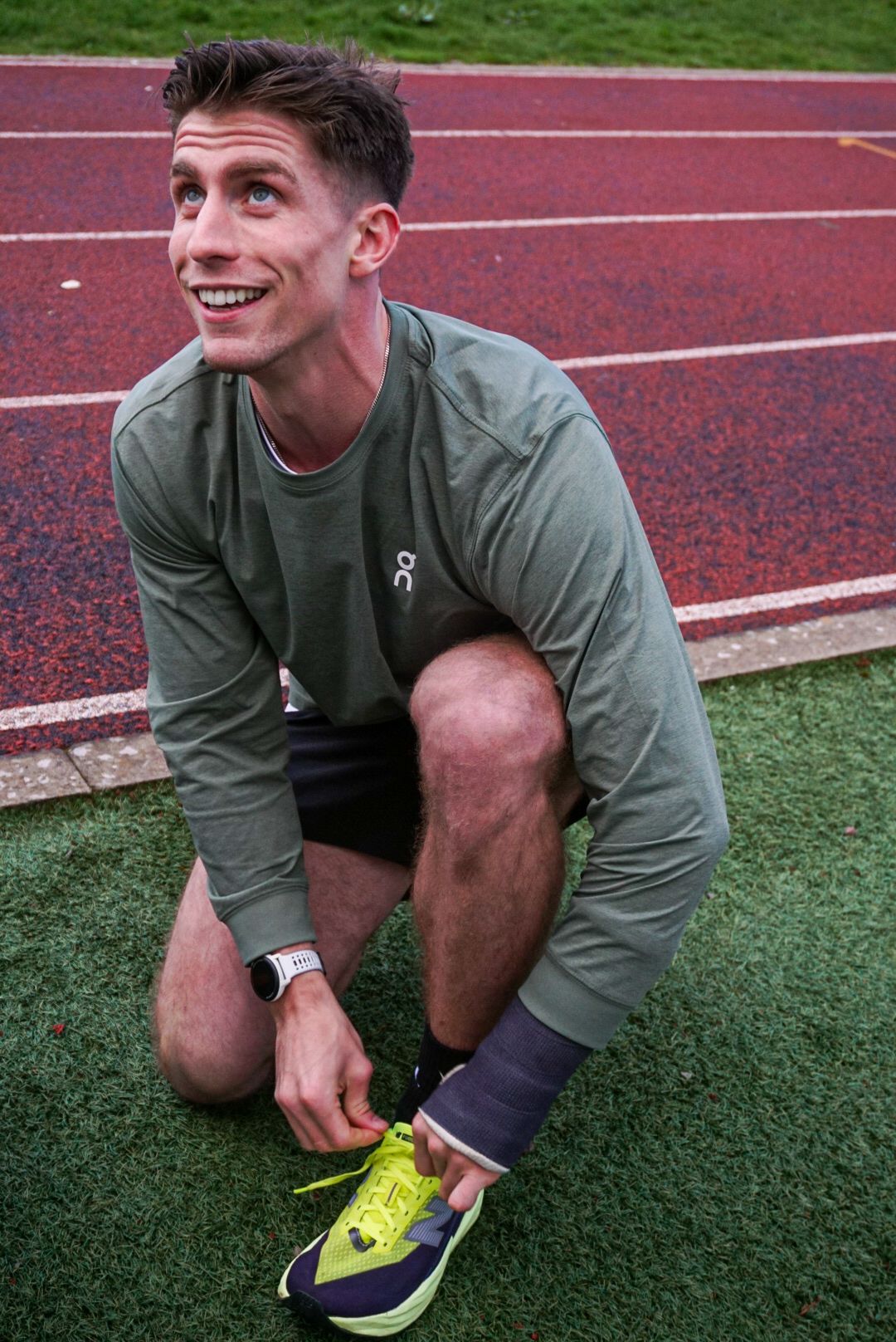 Smiling male runner tying bright yellow On running shoes on a red athletics track.