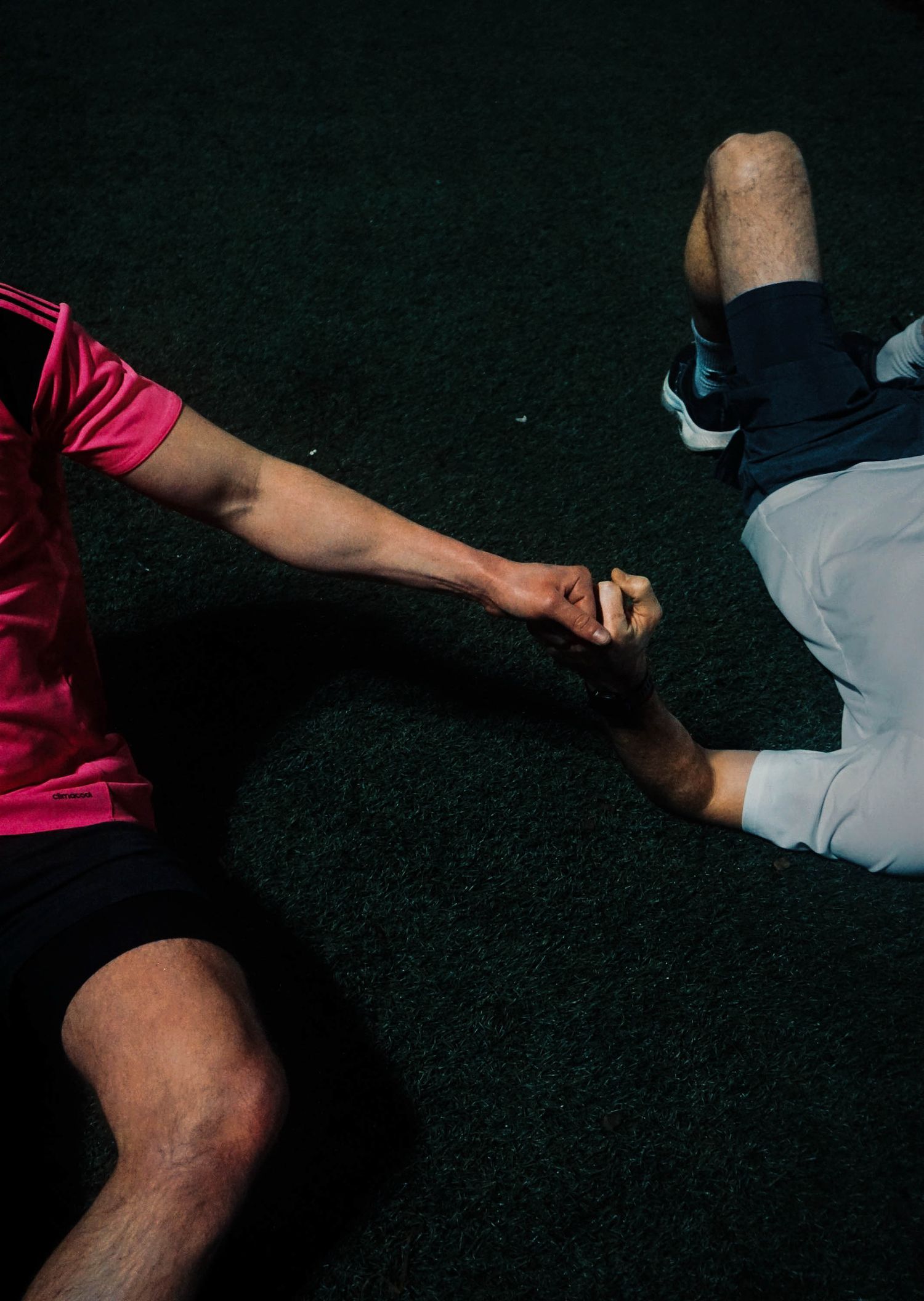 Two male athletes lying on artificial turf giving each other a fist bump after a game.