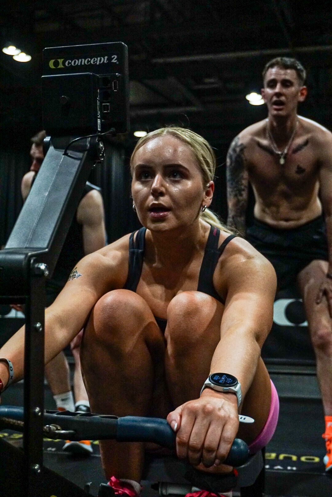 Focused female athlete rows on a Concept2 ergometer during a HYROX fitness competition.