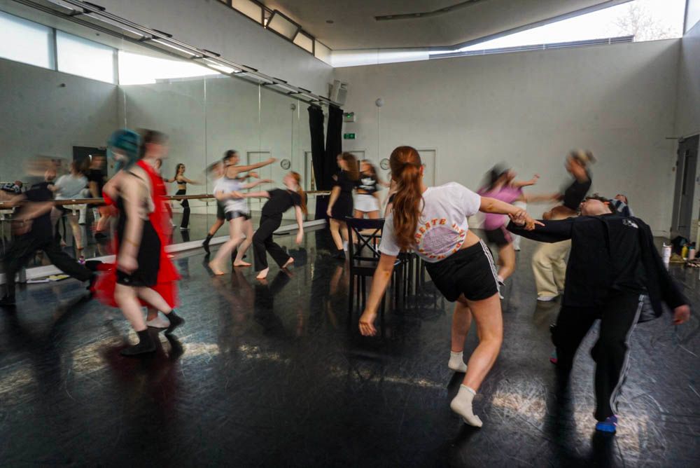 Dynamic group of dancers in motion during energetic contemporary dance rehearsal in mirrored studio.