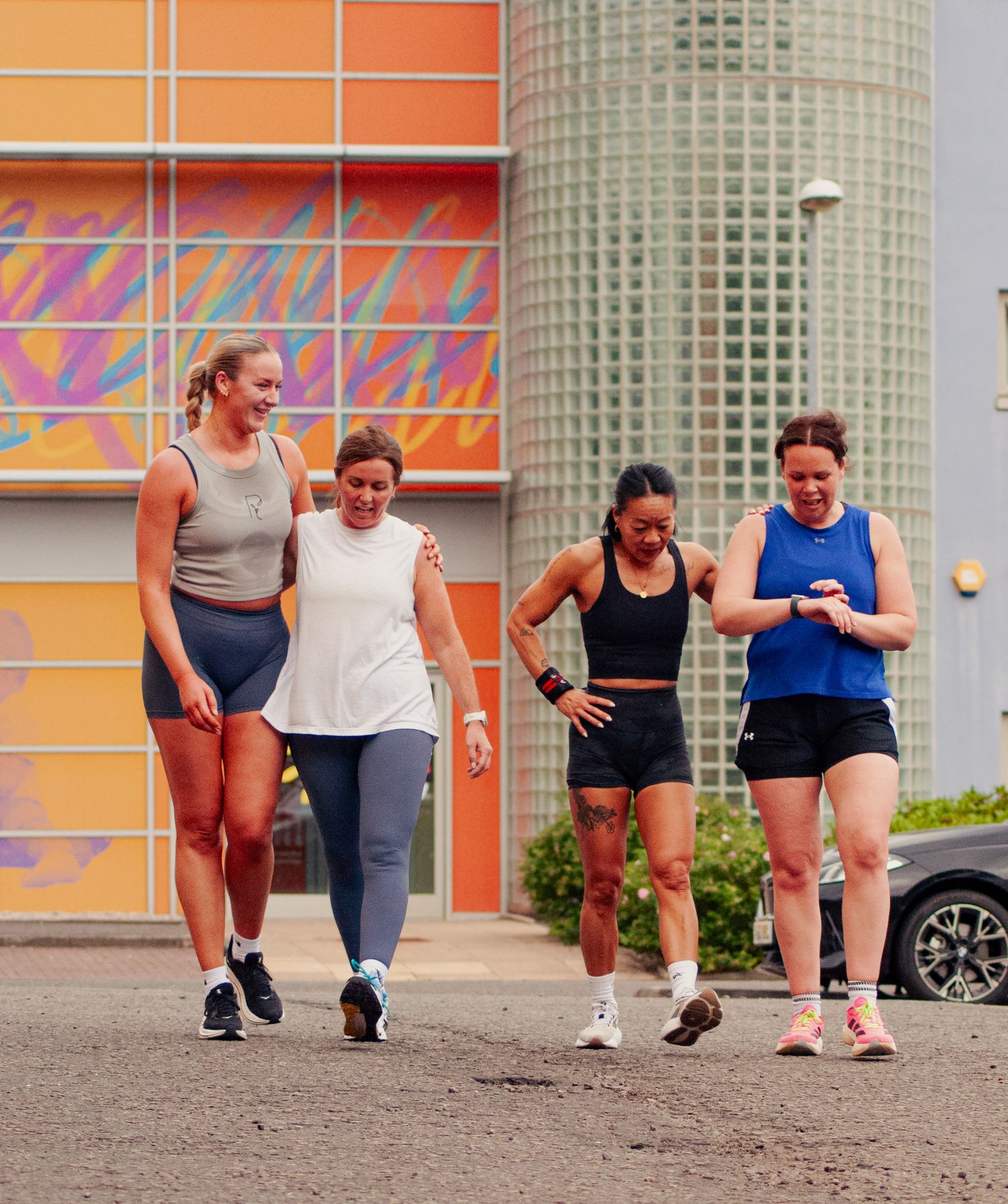 Four women in athletic wear walking together outdoors after a workout near a colorful mural wall.