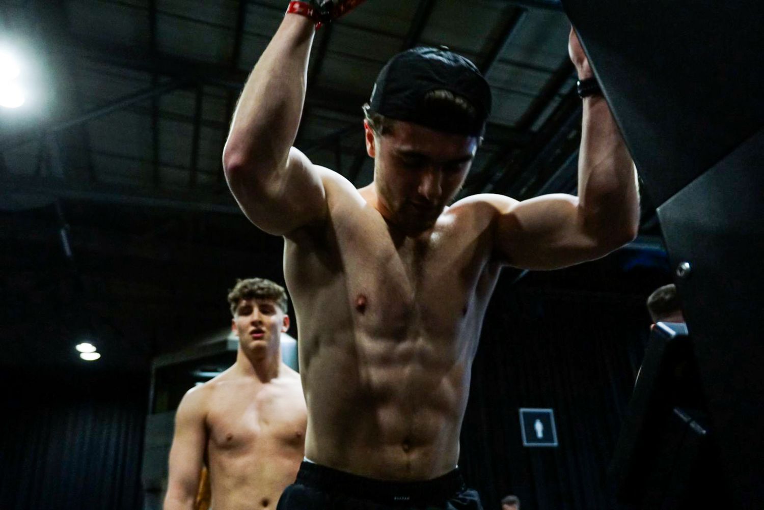 Muscular shirtless male athlete raising arms victoriously after completing a CrossFit competition workout.