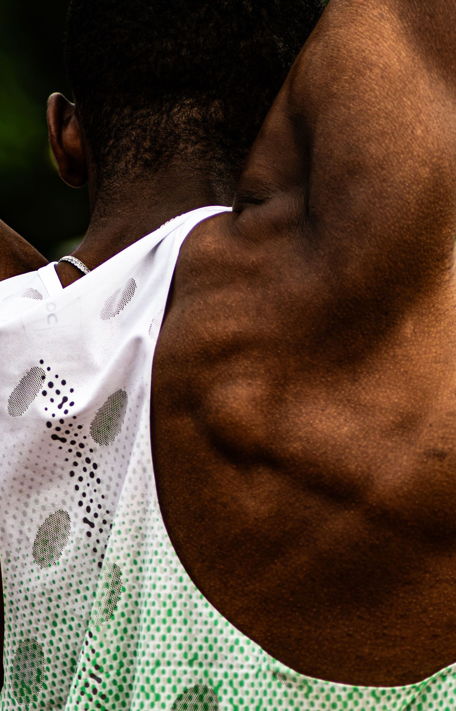 Close-up of a Black male athlete's muscular neck and shoulder wearing a white perforated running vest.