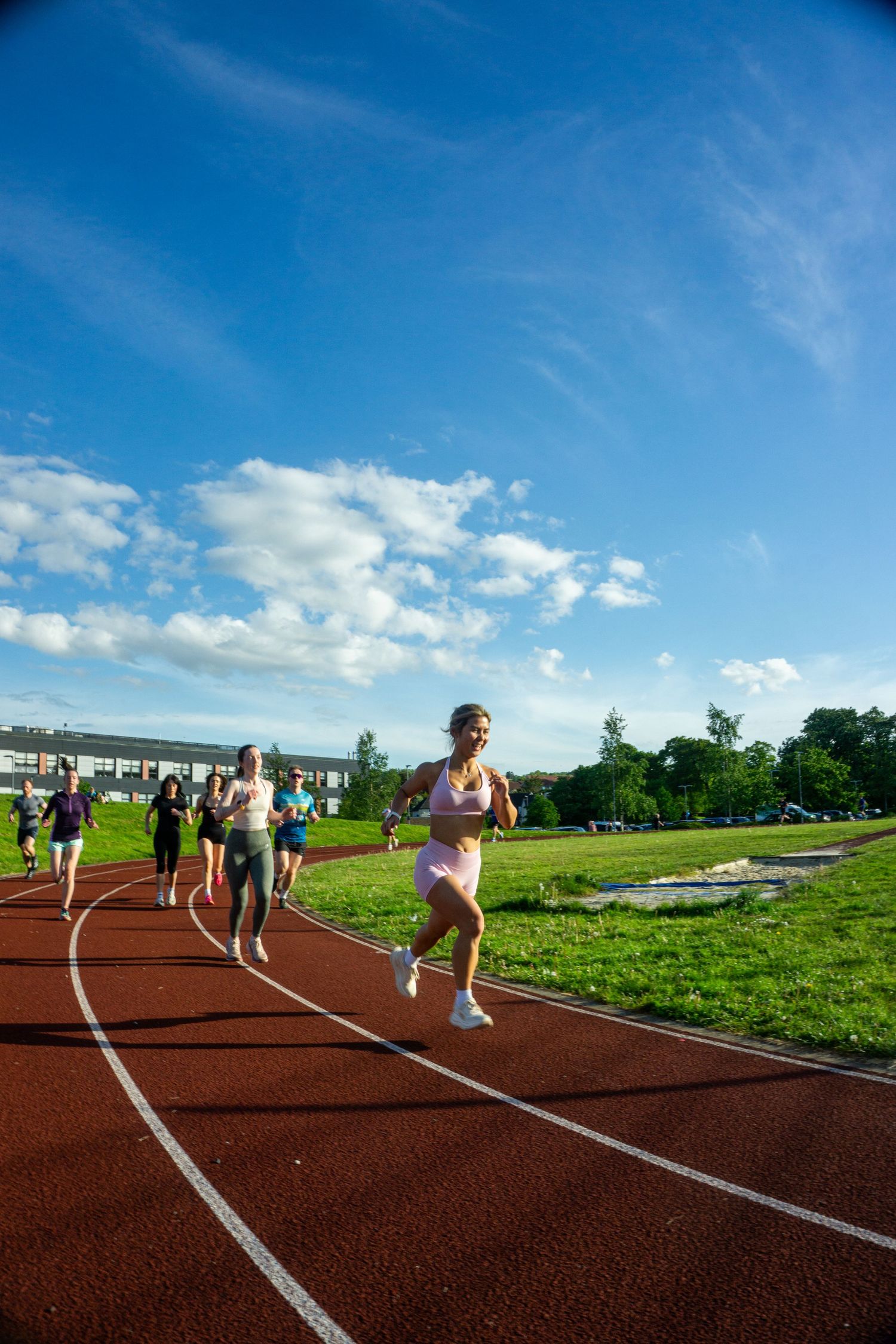 Group of runners led by woman in pink sports bra on red outdoor athletics track.