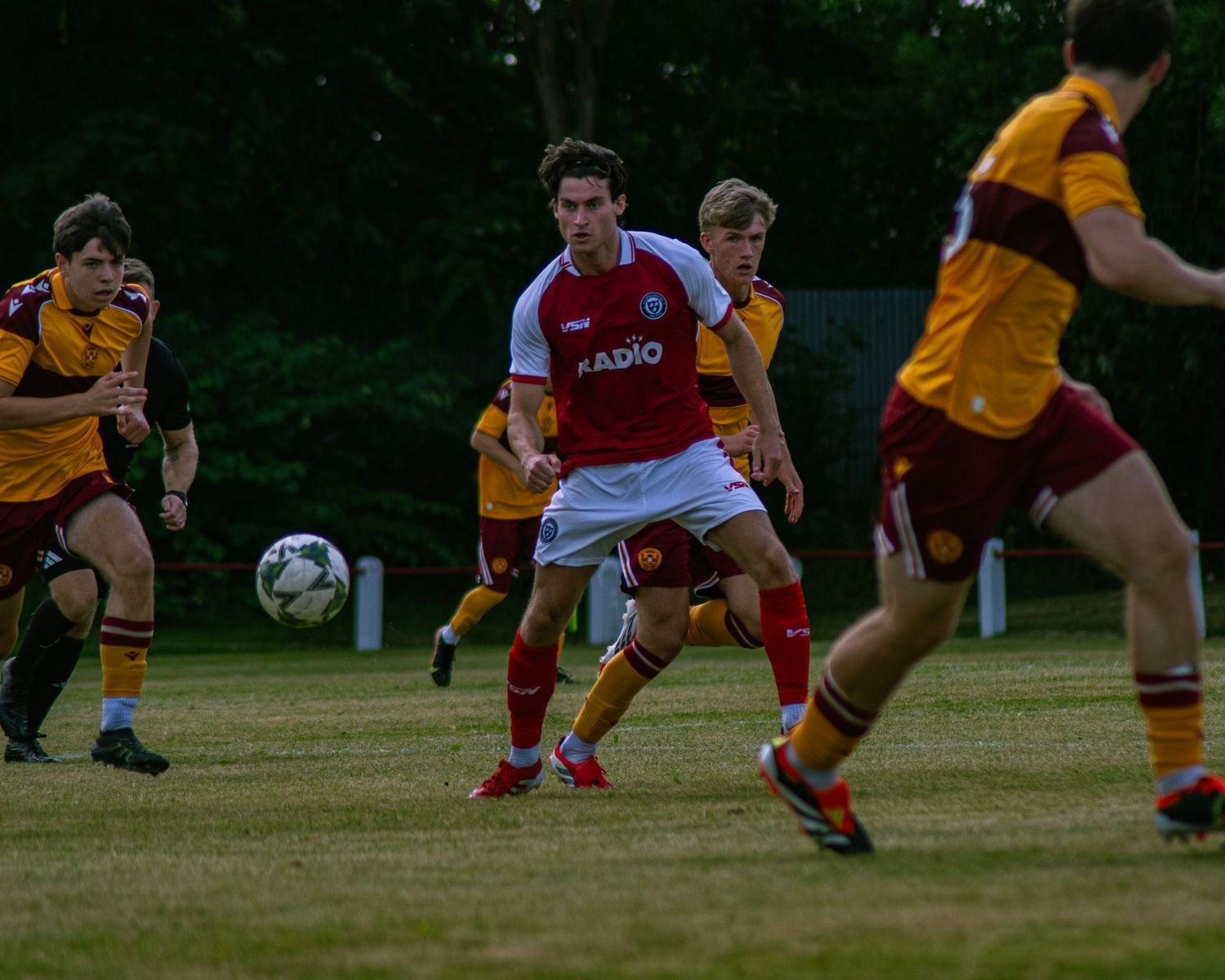 Soccer player in red and white RADIO jersey controls ball during competitive youth football match.