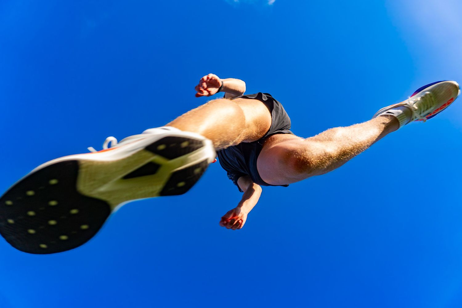 Dynamic low-angle view of a runner mid-stride against a vivid blue sky.