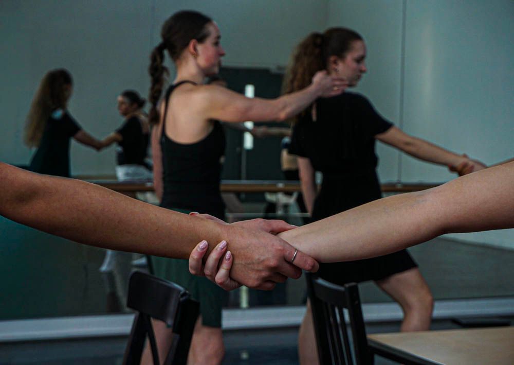 Close-up of dancers holding hands at ballet barre with mirror reflection in dance studio.