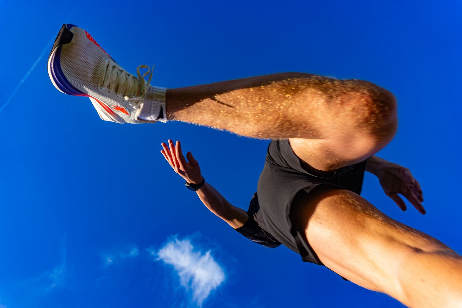 Low-angle view of a male sprinter launching off the ground against a vivid blue sky.