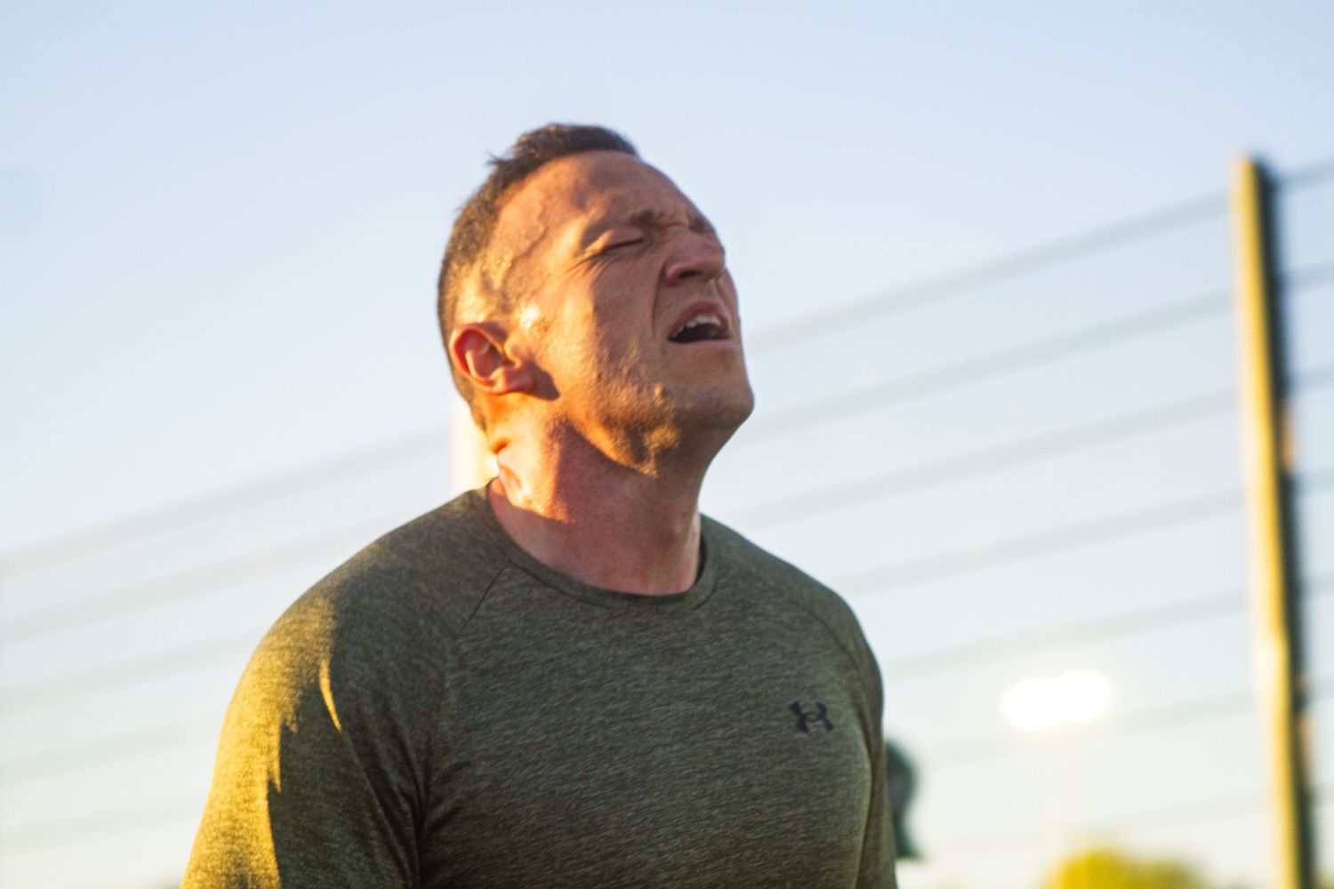 Male athlete in Under Armour shirt straining during intense outdoor track workout.
