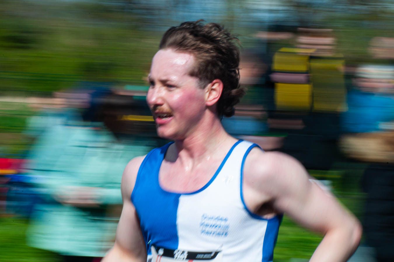 Male runner in blue vest competing in road race with motion blur background.