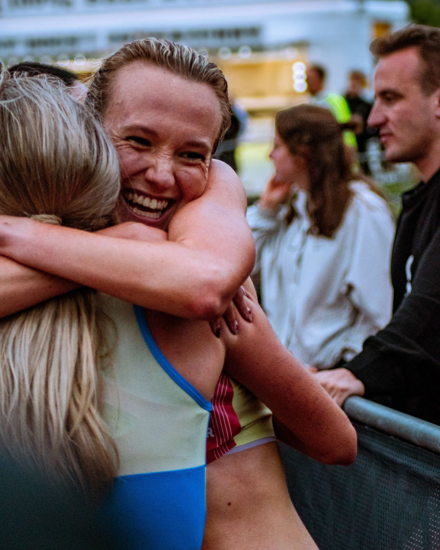 Two female athletes share a joyful embrace after a track and field competition, smiling with excitement.