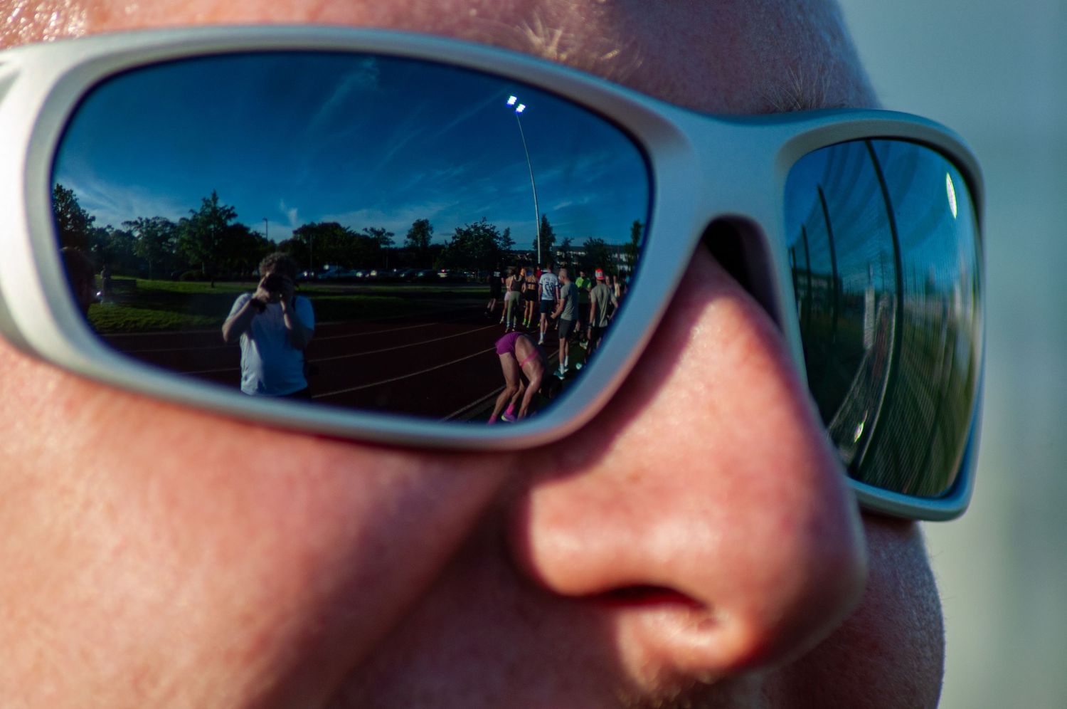 Close-up of sunglasses reflecting a group of people on a sports track in bright sunlight.
