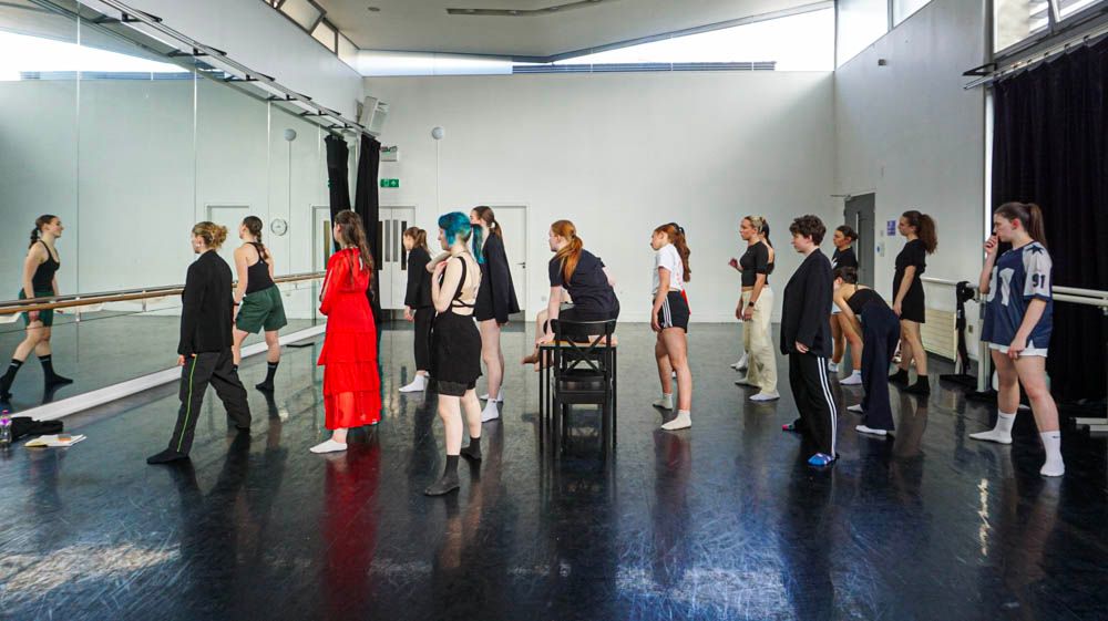Dance students standing in a line during a ballet barre class in a mirrored studio.