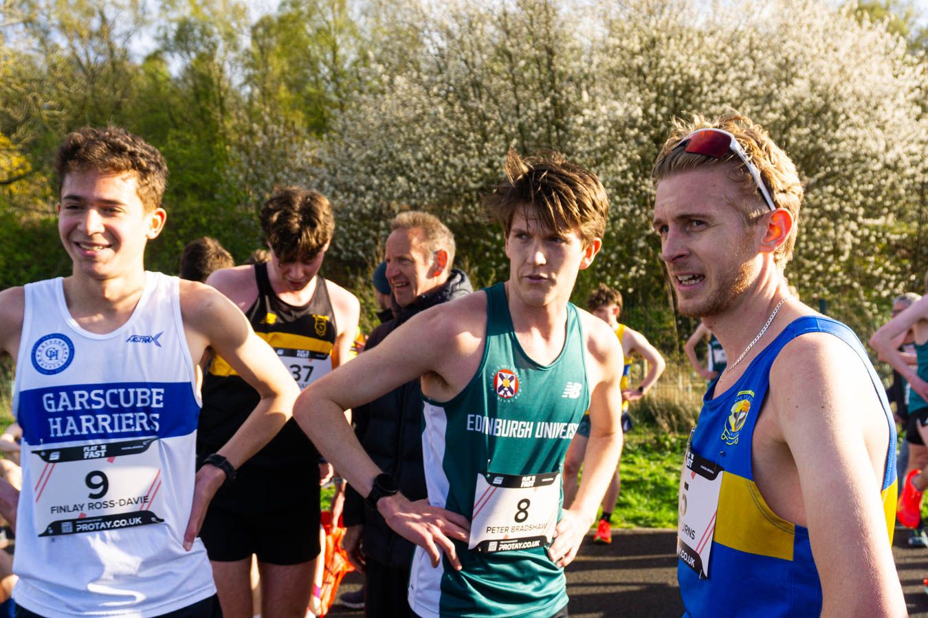 Three male runners in athletic gear smiling and chatting before a road race event.