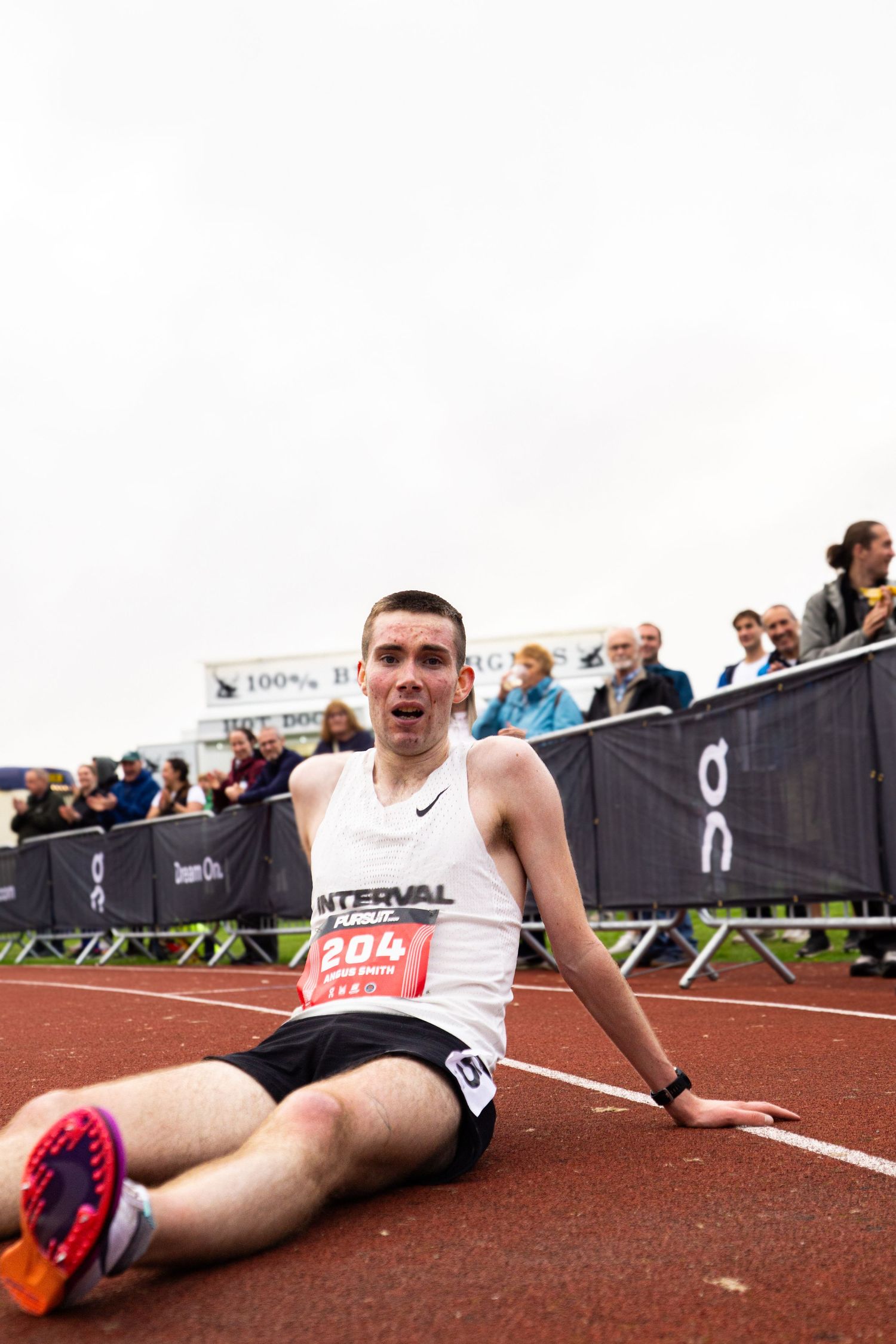 Exhausted runner wearing bib number 204 sits on track after finishing race at athletic competition.