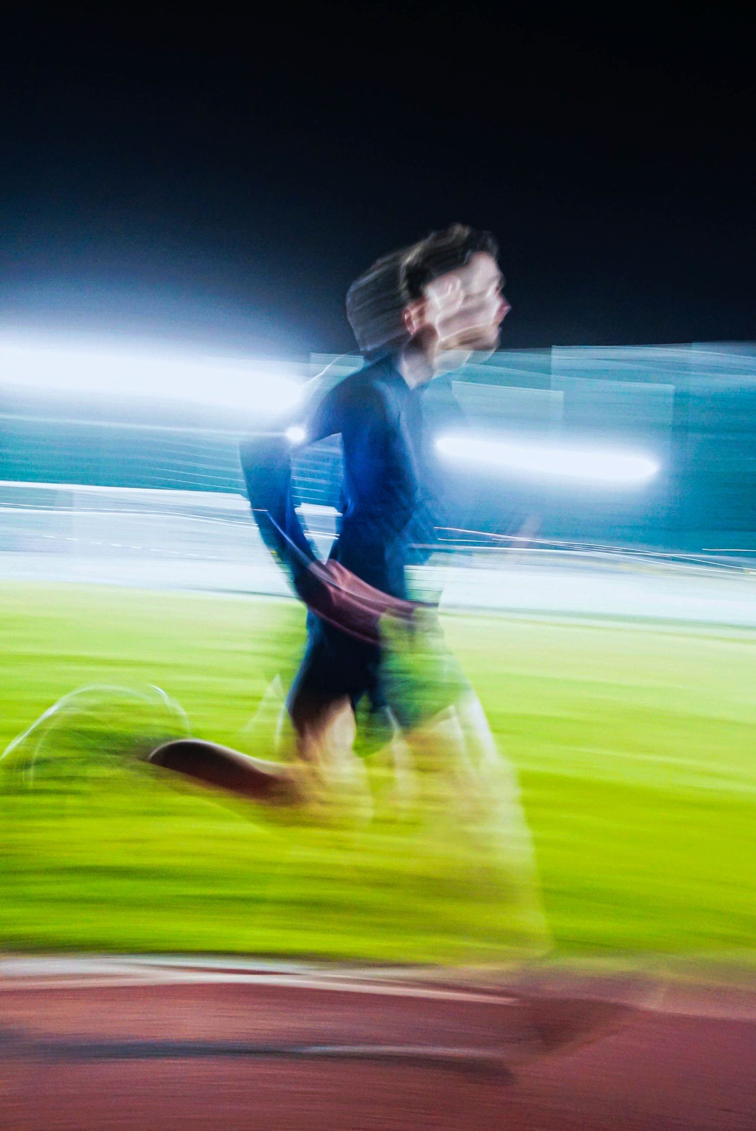 Blurred motion shot of a runner sprinting on a track at night with stadium lights streaking across the frame.