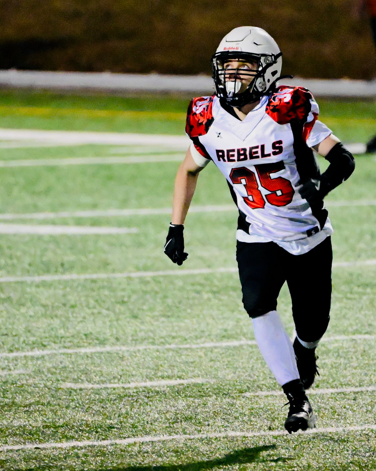 Youth football player wearing Rebels jersey number 35 runs on turf field during a game.