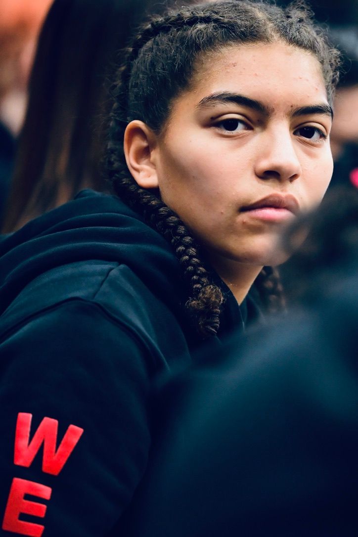 A young female athlete with braided hair wearing a black hoodie looks seriously at the camera.