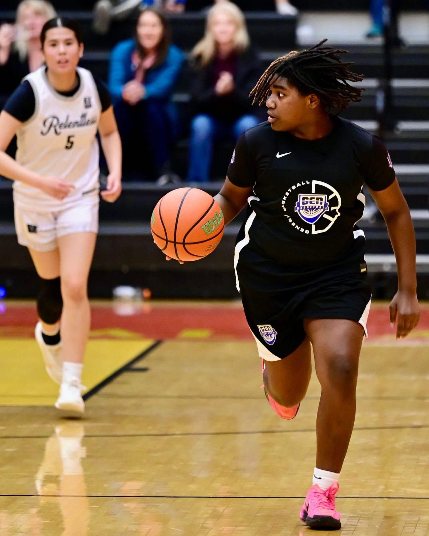 Female basketball player in black uniform dribbling ball during indoor basketball game.