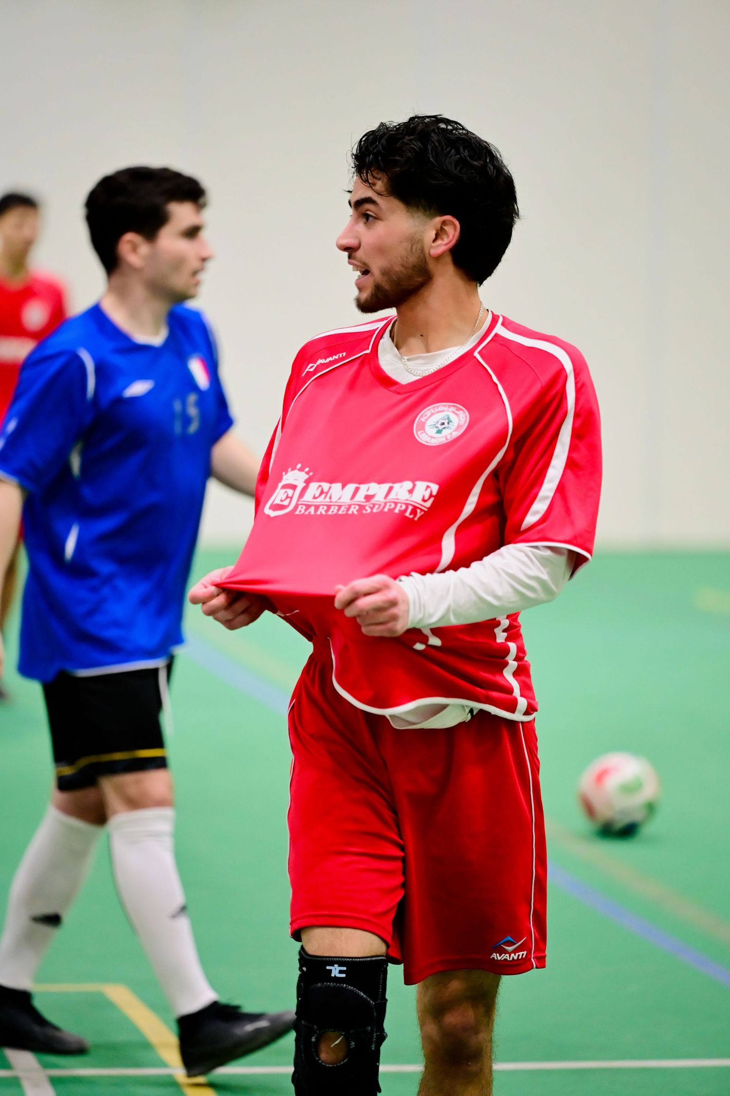A male soccer player in a red Empire jersey holds his shirt during an indoor futsal match.