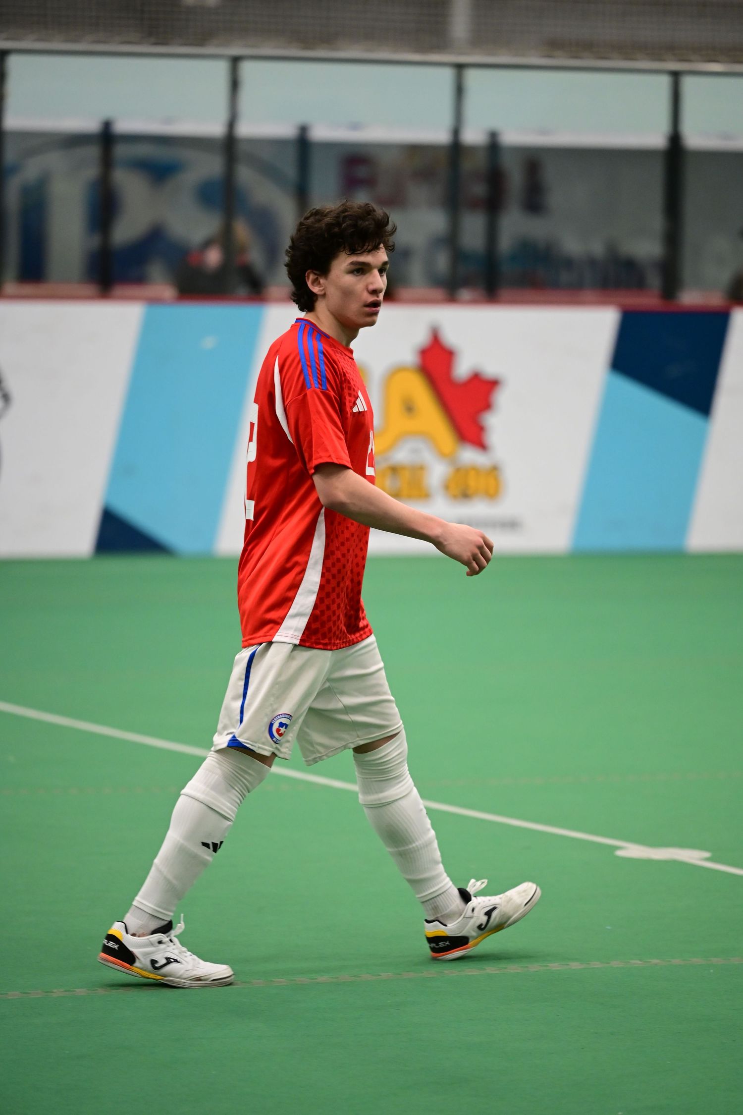 Chile youth soccer player in red uniform walks on indoor turf during tournament.
