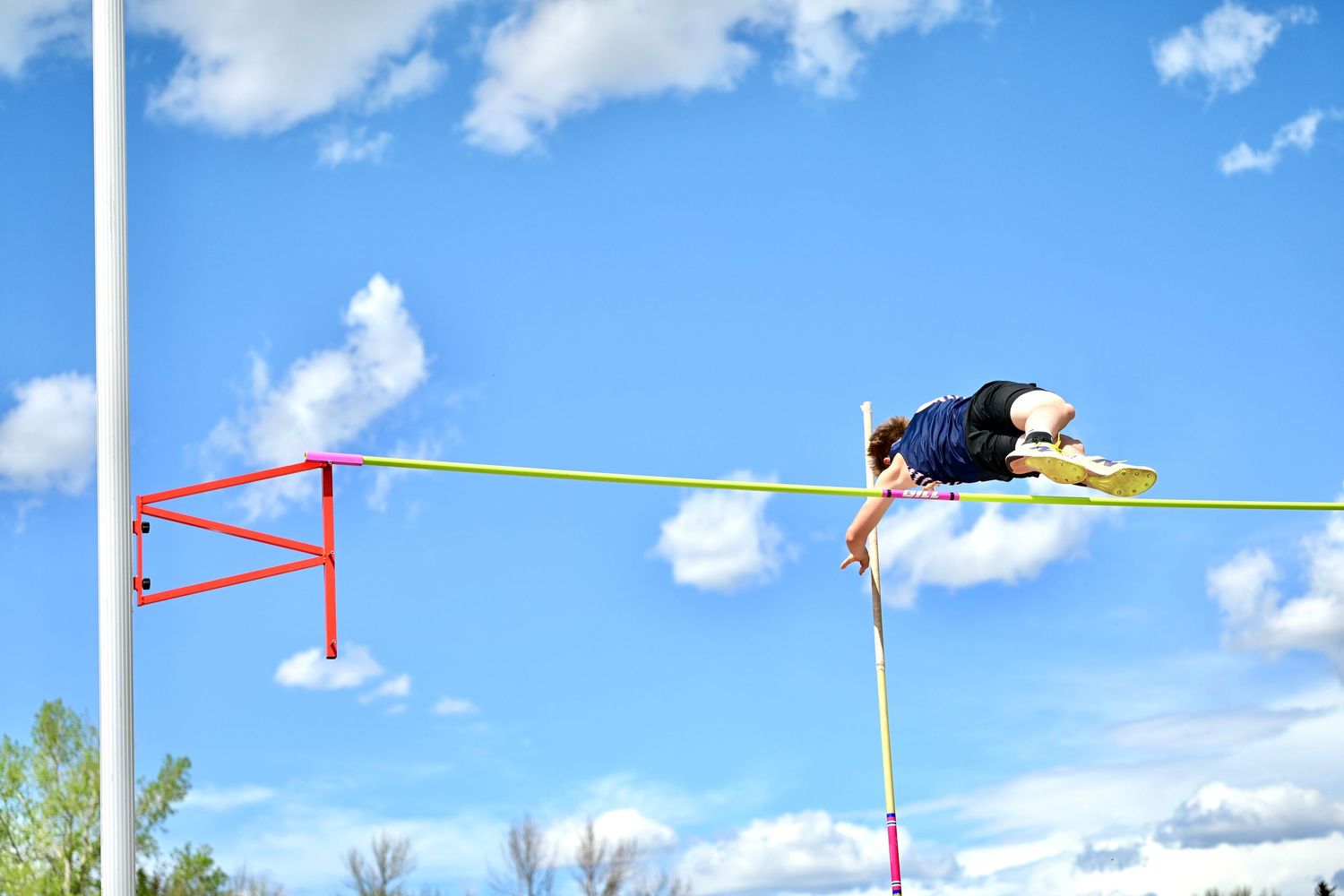 Athlete clears the bar during a pole vault competition under blue sky.
