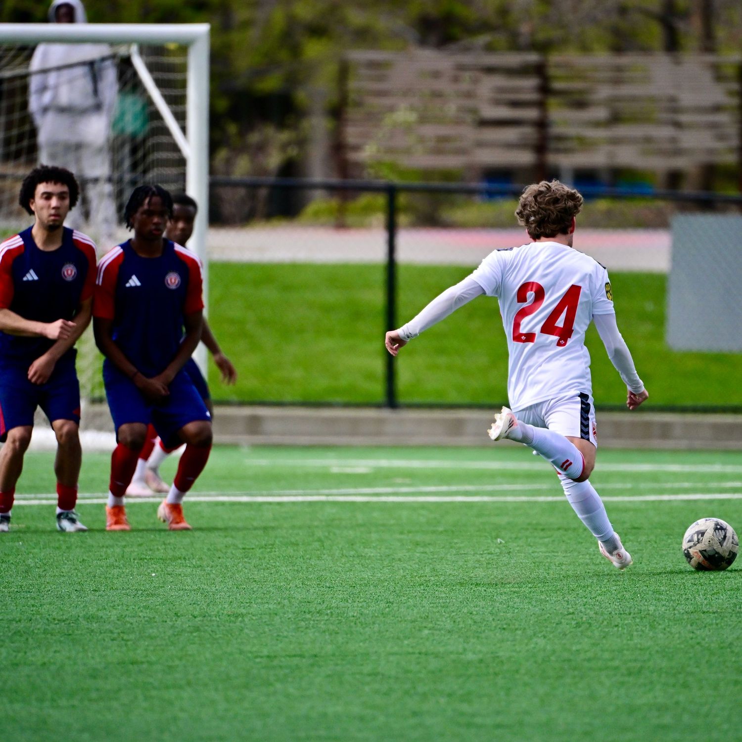 Soccer player in white number 24 jersey kicking ball on green turf during match.