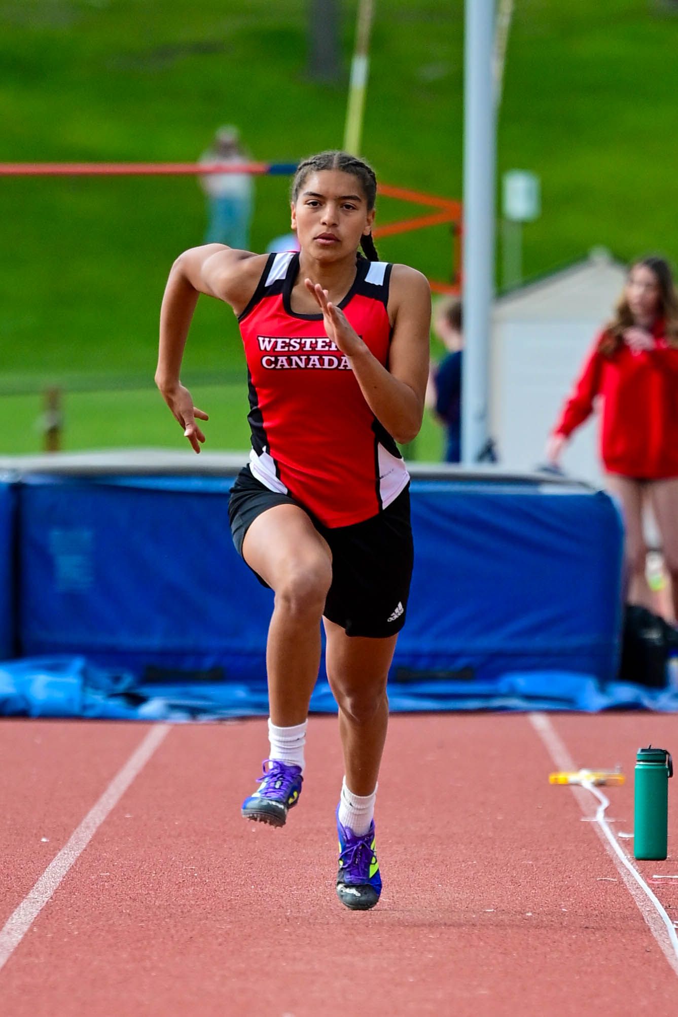 Female sprinter in Western Canada red uniform accelerating down track lane during outdoor athletics meet.