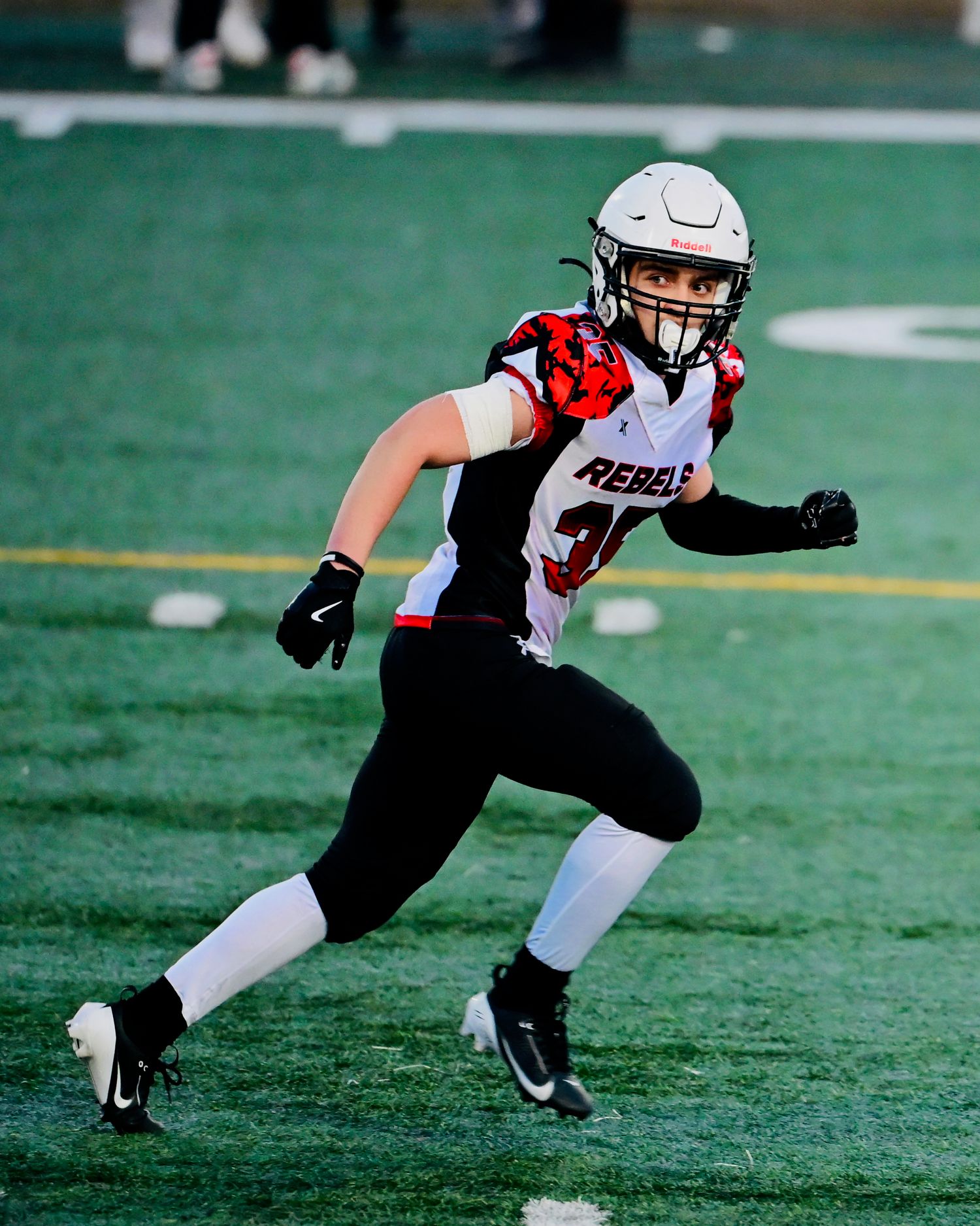 Youth football player wearing Rebels helmet and uniform running on green turf field.