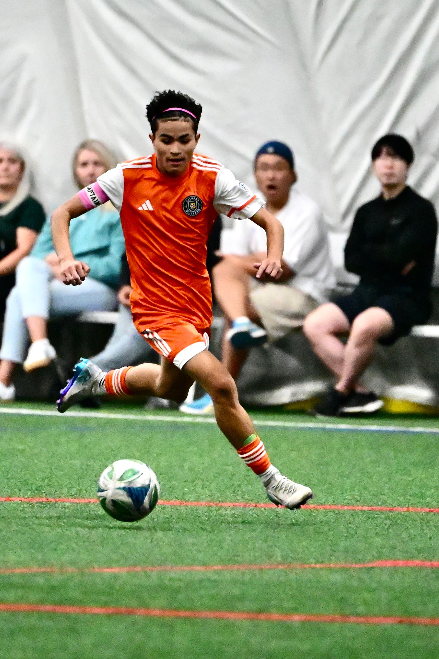 Soccer player in orange Adidas jersey striking ball on indoor turf field.
