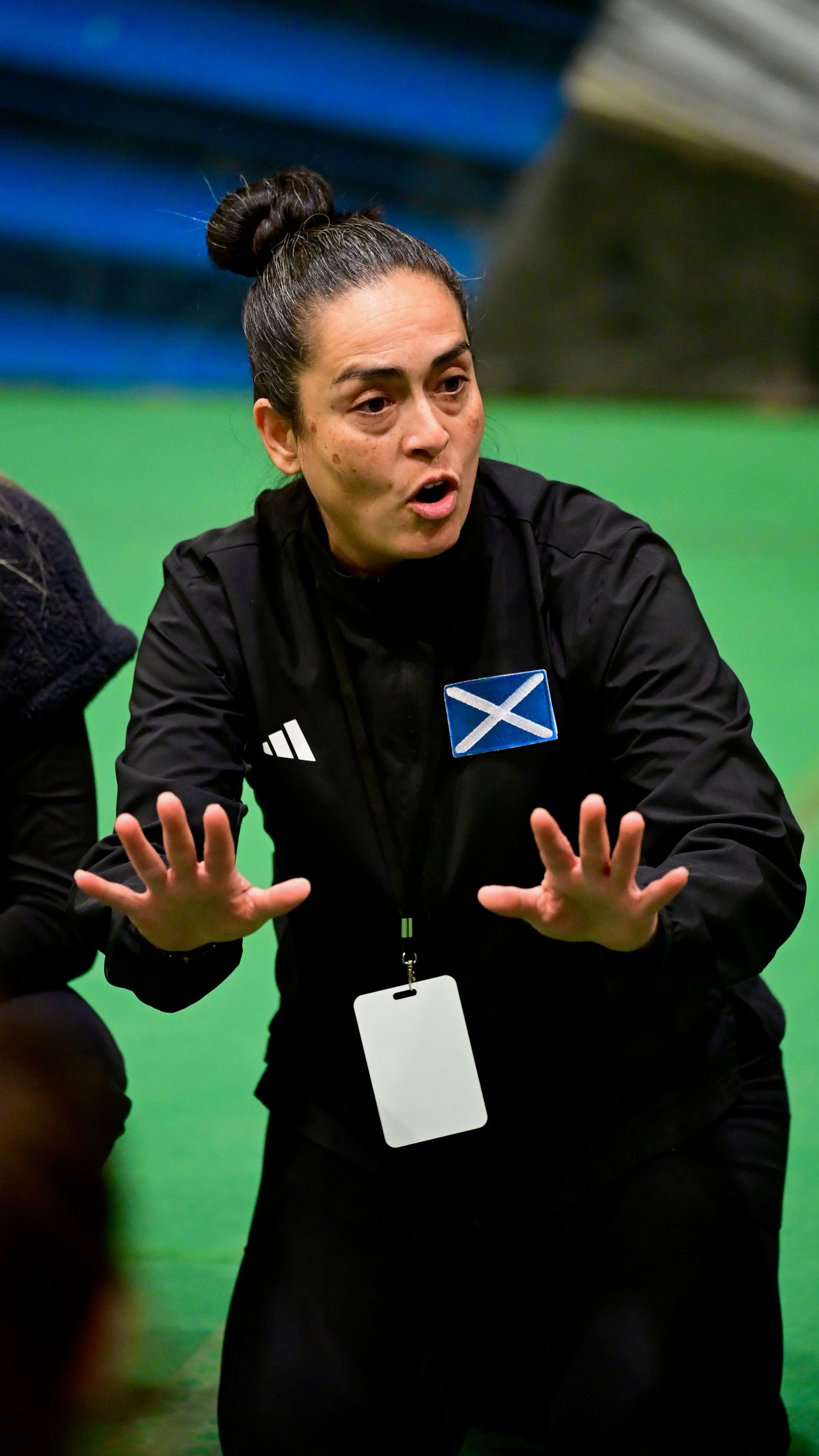 A female coach wearing a Scotland badge on her black Adidas jacket gestures during a sports briefing.