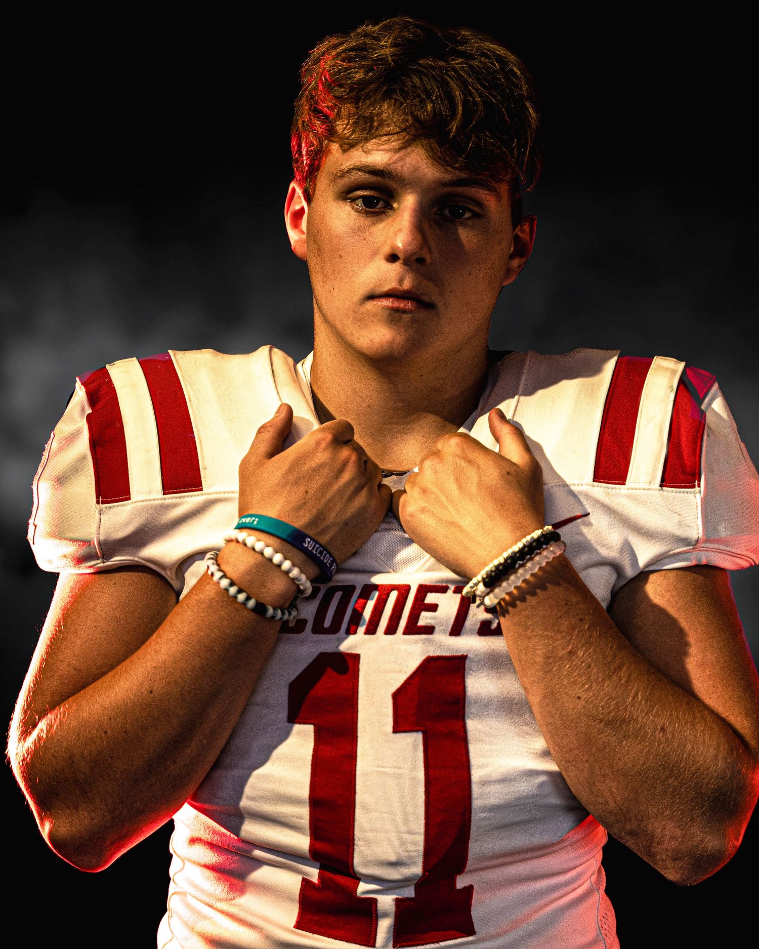 High school football player wearing white Comets jersey number 11 poses confidently under dramatic lighting.
