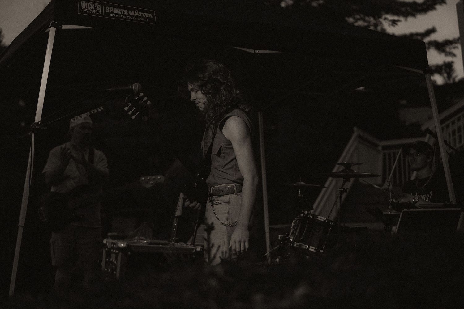 A vintage-toned black and white photo of two musicians performing on an outdoor stage at dusk.