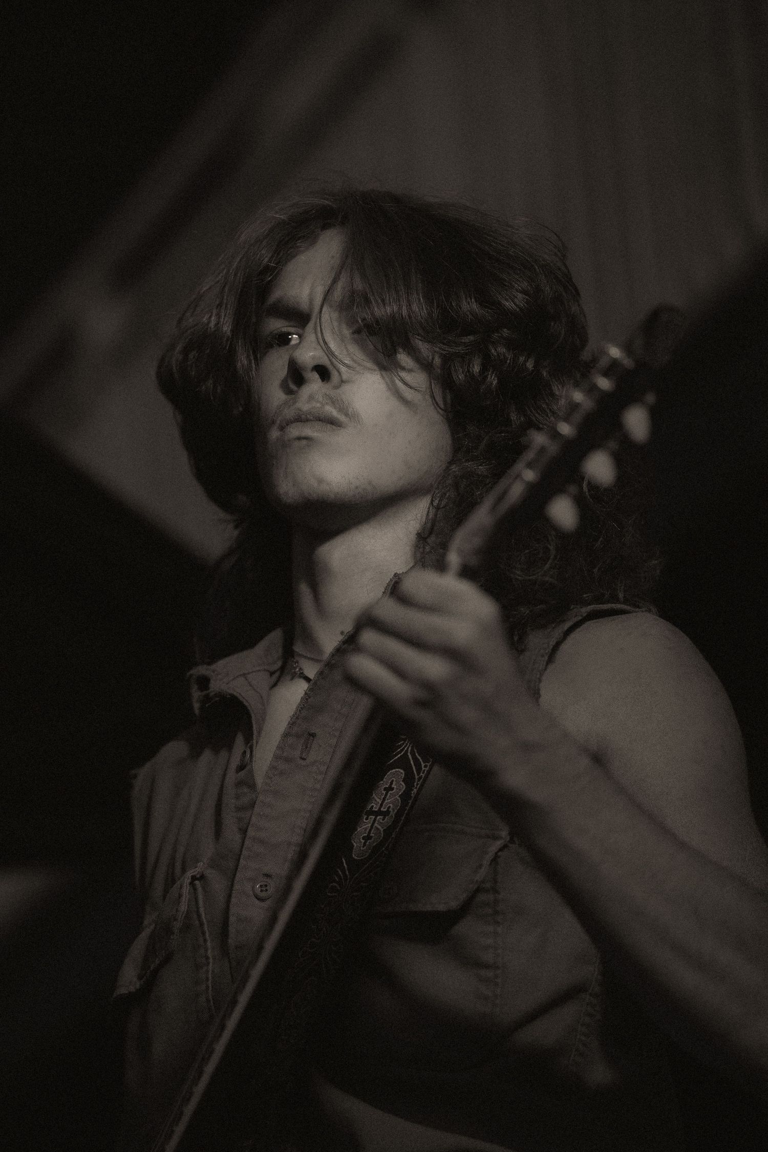 A black and white close-up of a long-haired musician intensely playing an electric guitar on stage.